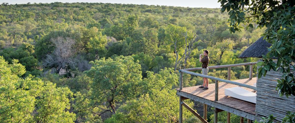Leopard Hills lodge guest on corner of wooden deck overlooking a lush green wilderness.