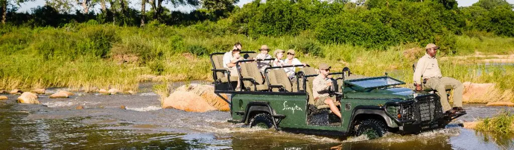 Singita Game Drive vehicle splashing through water in Sabi Sand by Ross Couper