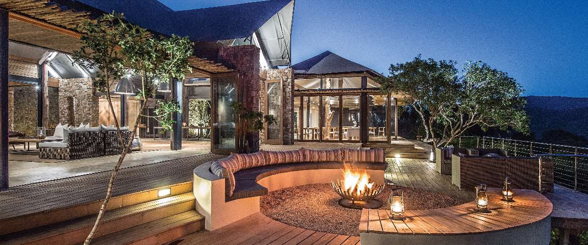 Opulent open plan lodge dining room and lounge leading onto open air firepit with comfortable seating around it.