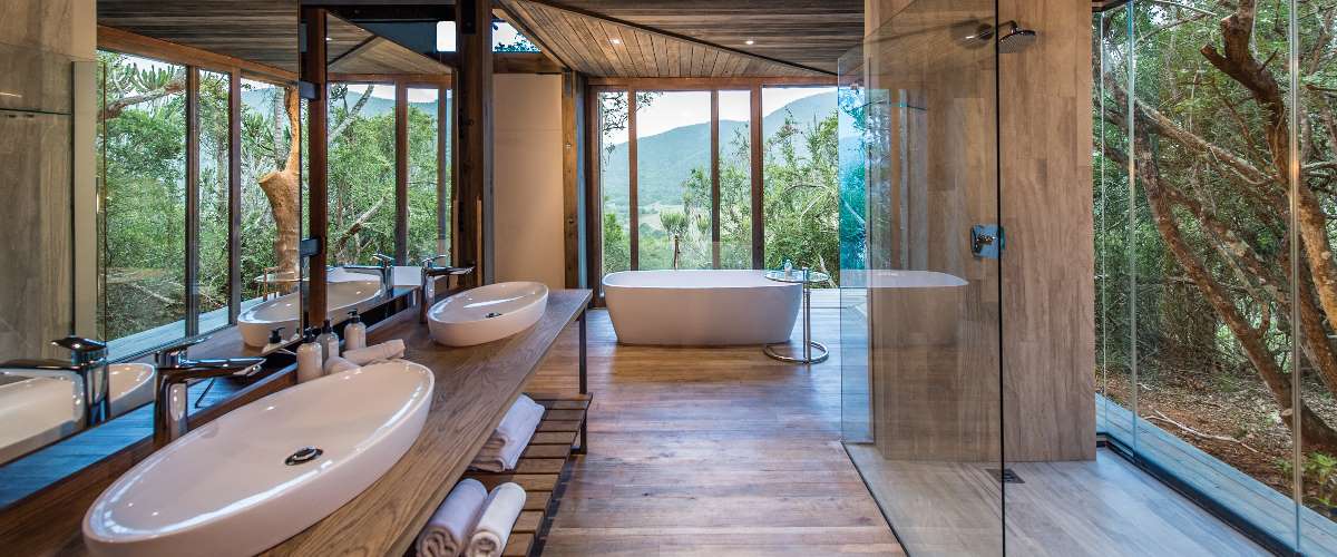 Spacious and airy Settlers Drift bathroom with indoor and outdoor showers, double vanity, bathtub and glass walls for views across Kariega bushveld.